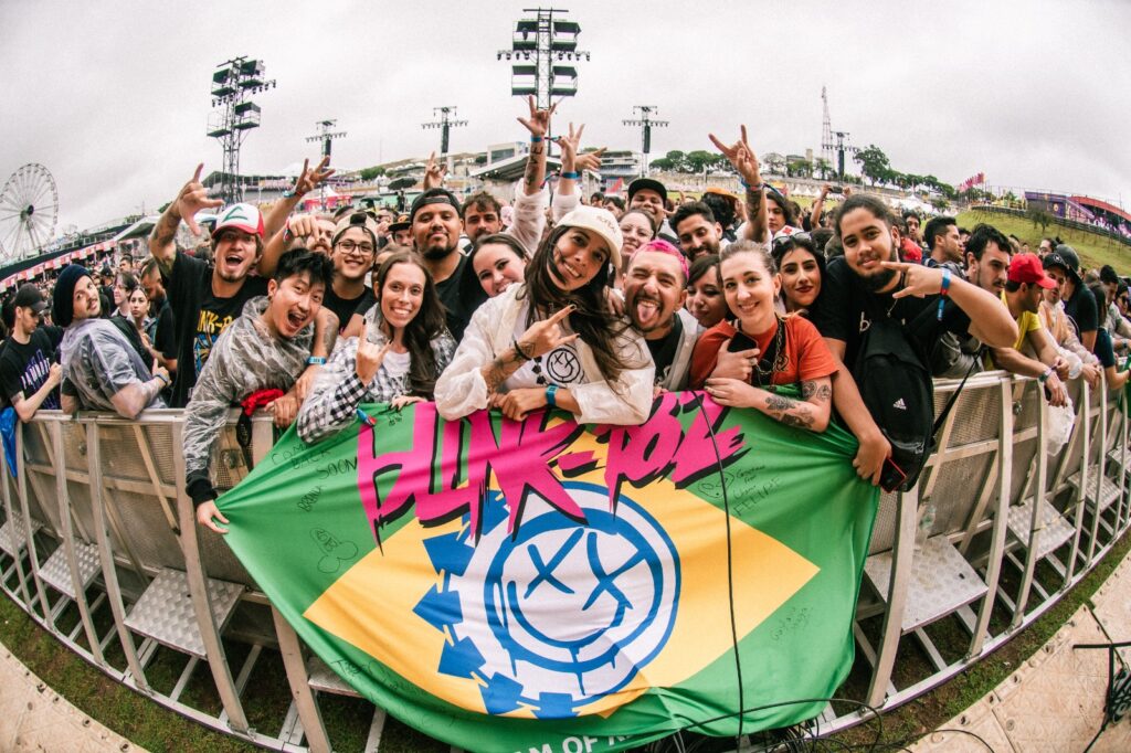 Fãs na grade do Lollapalooza com bandeira do Brasil customizada com o logo do blink-182